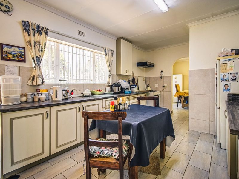 A functional kitchen featuring built-in cabinetry, laminate countertops, tiled backsplash, and tiled flooring, with an adjacent archway leading to a dining area.