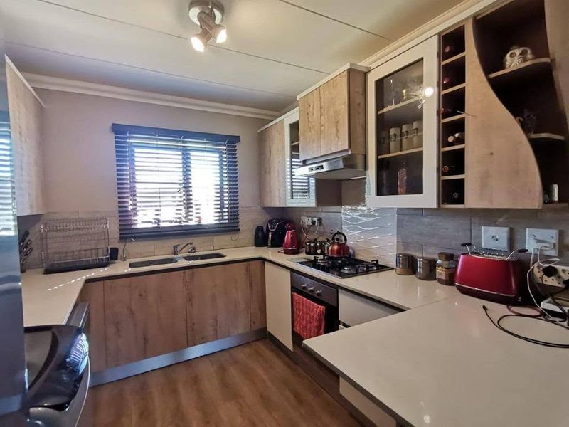 A well-appointed kitchen featuring wood-finish cabinetry, stone countertops, a gas hob with extractor, and integrated storage including a wine rack.
