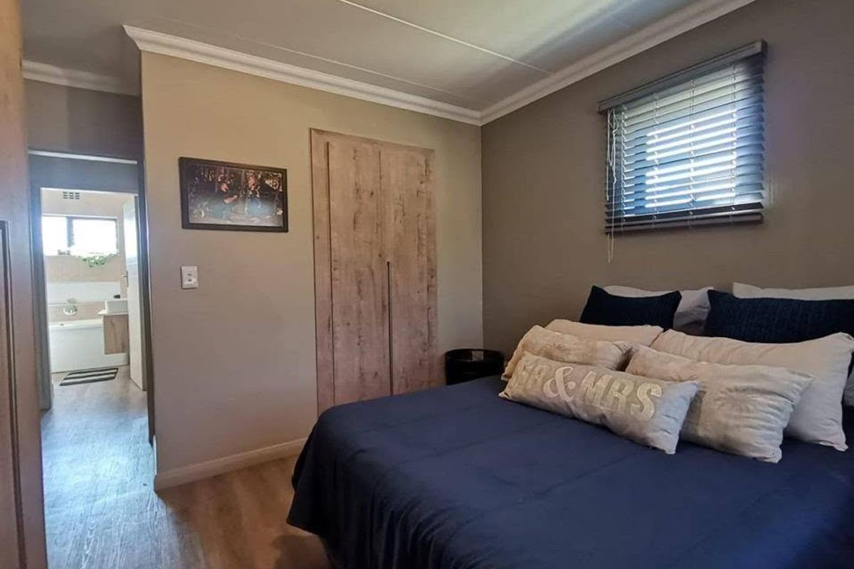 A well-maintained bedroom featuring laminate flooring, built-in wardrobes, and venetian blinds, with an adjoining bathroom visible through the doorway.