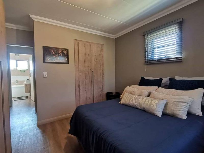 A well-maintained bedroom featuring laminate flooring, built-in wardrobes, and venetian blinds, with an adjoining bathroom visible through the doorway.