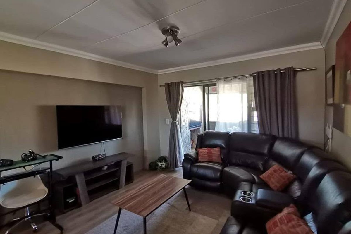 A comfortable living room featuring laminate flooring, coved ceilings, and a sliding glass door providing access to the outdoor area.