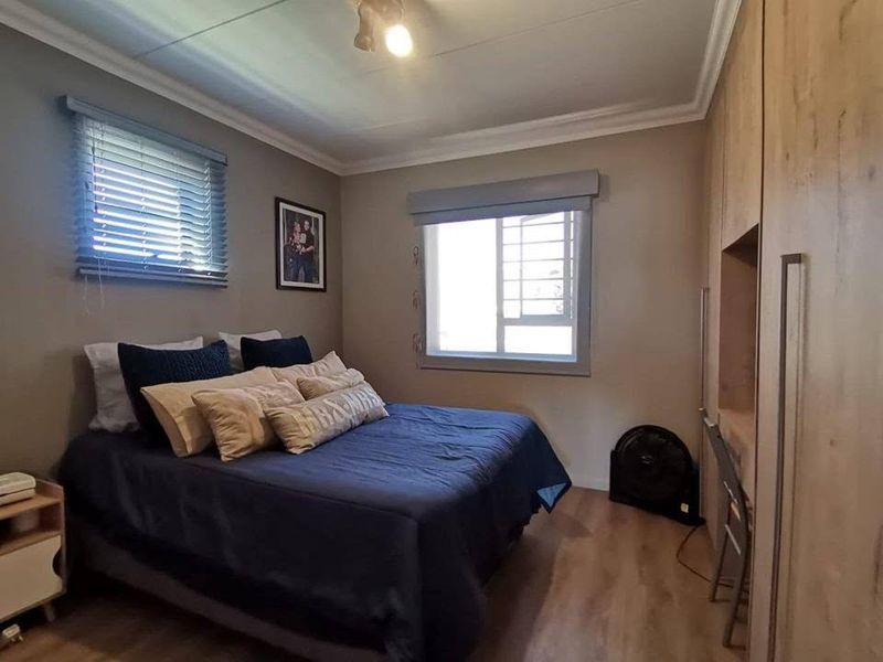 A well-maintained bedroom featuring laminate flooring, built-in cupboards, and dual window treatments including venetian and roller blinds.