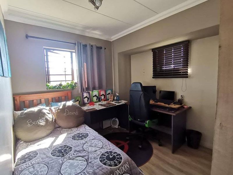 A functional bedroom featuring laminate flooring, a window with security bars, and venetian blinds, offering a practical layout for sleeping and study.