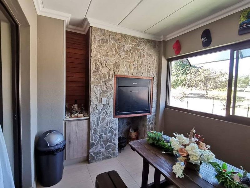 Covered patio area featuring a built-in braai with stone cladding, tiled flooring, and large sliding windows overlooking the garden.