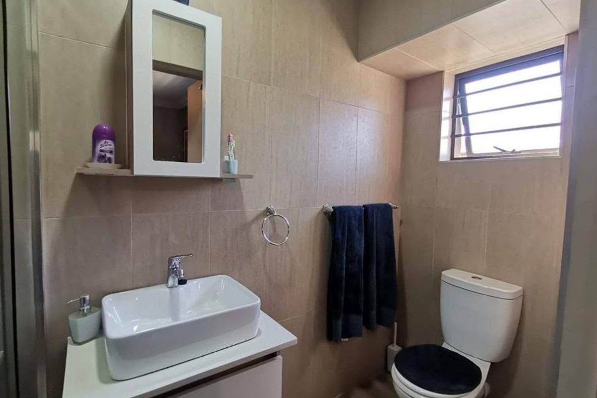 A modern bathroom featuring a vessel sink on a vanity cabinet, a wall-mounted mirror cabinet, and neutral wall tiling.