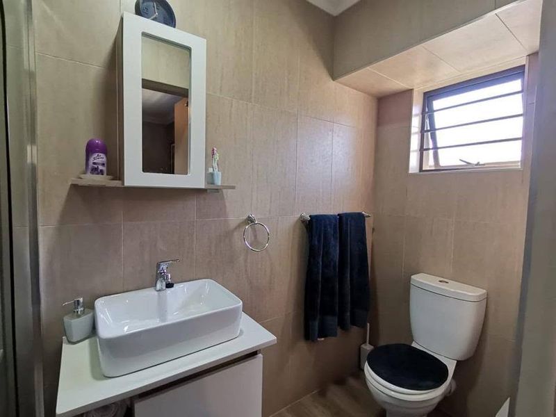 A modern bathroom featuring a vessel sink on a vanity cabinet, a wall-mounted mirror cabinet, and neutral wall tiling.