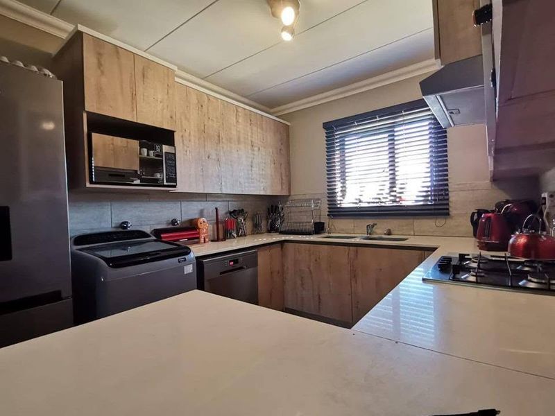 A well-appointed kitchen featuring modern wood-finish cabinetry, stone countertops, a gas hob, extractor fan, and integrated microwave, offering a functional and contemporary cooking space.
