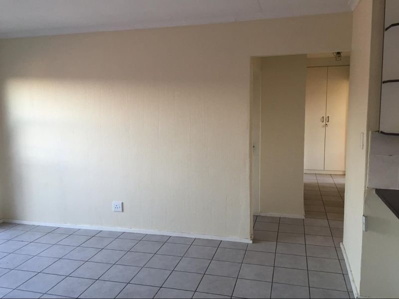 An empty living area featuring neutral tiled flooring and a clear transition into a hallway with built-in storage cupboards.