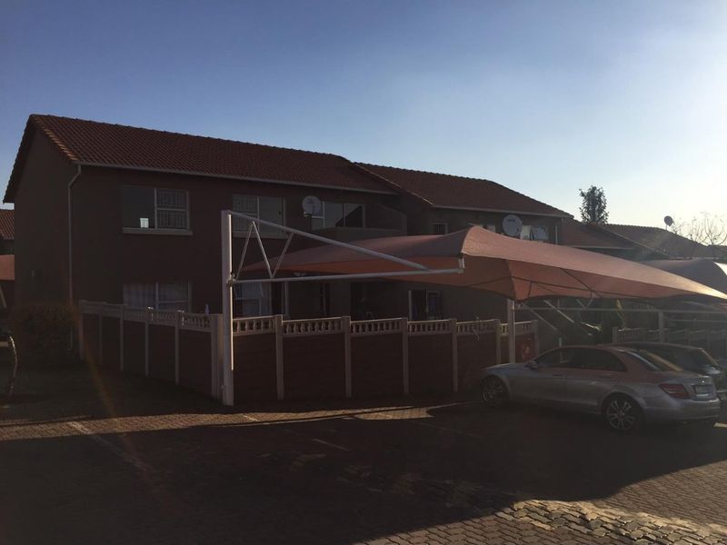 Exterior view of the apartment building featuring a paved driveway, a large shade sail structure, and perimeter precast concrete walling.