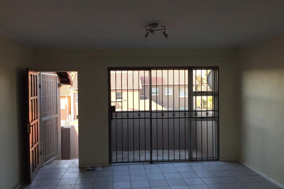 An empty living room featuring tiled flooring, a security gate, and a sliding door leading to an outdoor area.