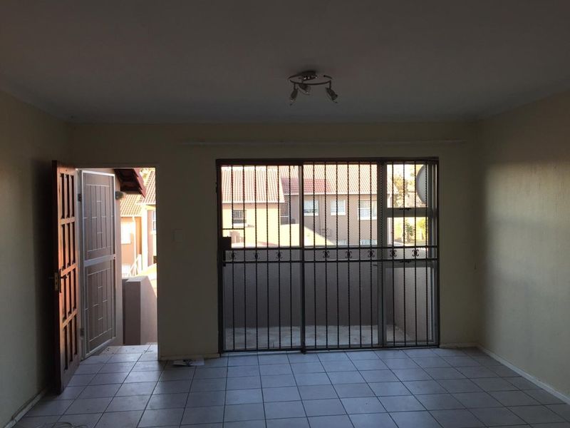 An empty living room featuring tiled flooring, a security gate, and a sliding door leading to an outdoor area.