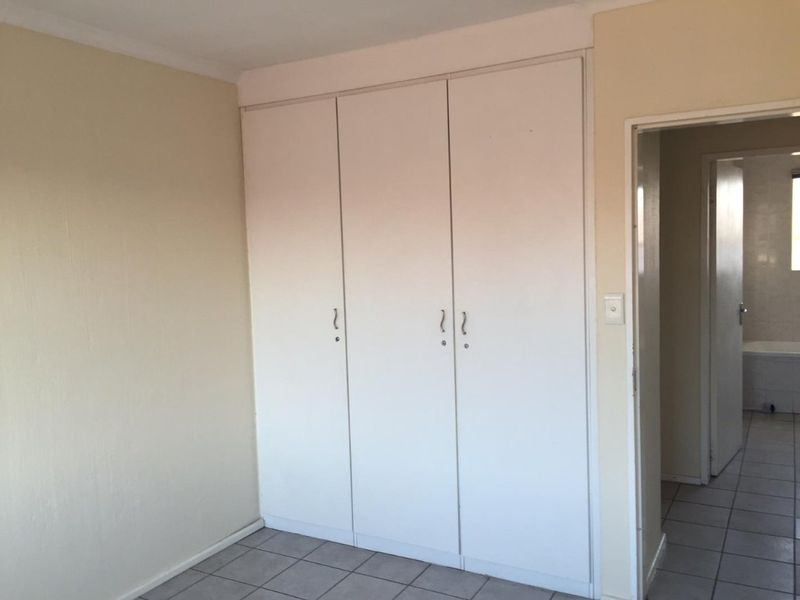 A clean, empty bedroom featuring built-in cupboards, tiled flooring, and neutral wall finishes, with an adjacent view into a tiled bathroom.