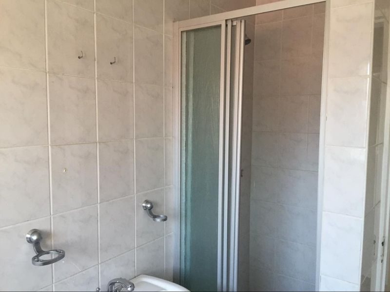 A functional bathroom featuring tiled walls, a shower enclosure, and wall-mounted fixtures, currently in need of cosmetic updates.