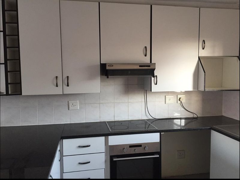 A functional kitchen featuring white cabinetry, dark countertops, a built-in oven, and an electric hob with a tiled backsplash.