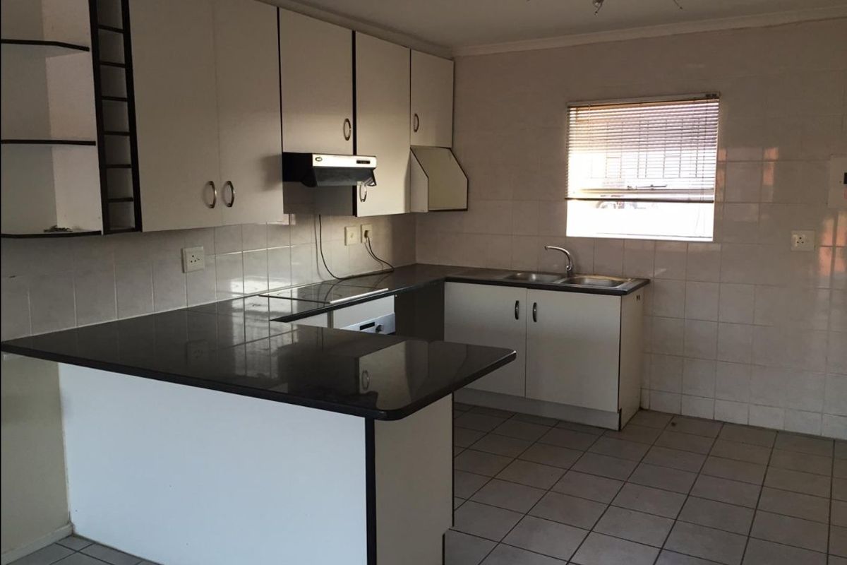 A functional kitchen featuring white cabinetry, dark countertops, tiled flooring, and a tiled splashback, offering a clean and practical layout for renovation.