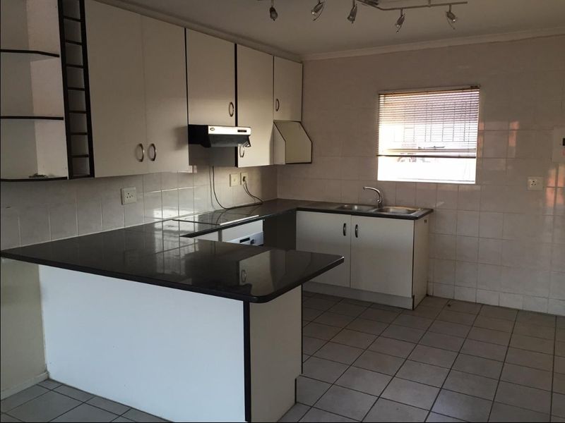A functional kitchen featuring white cabinetry, dark countertops, tiled flooring, and a tiled splashback, offering a clean and practical layout for renovation.