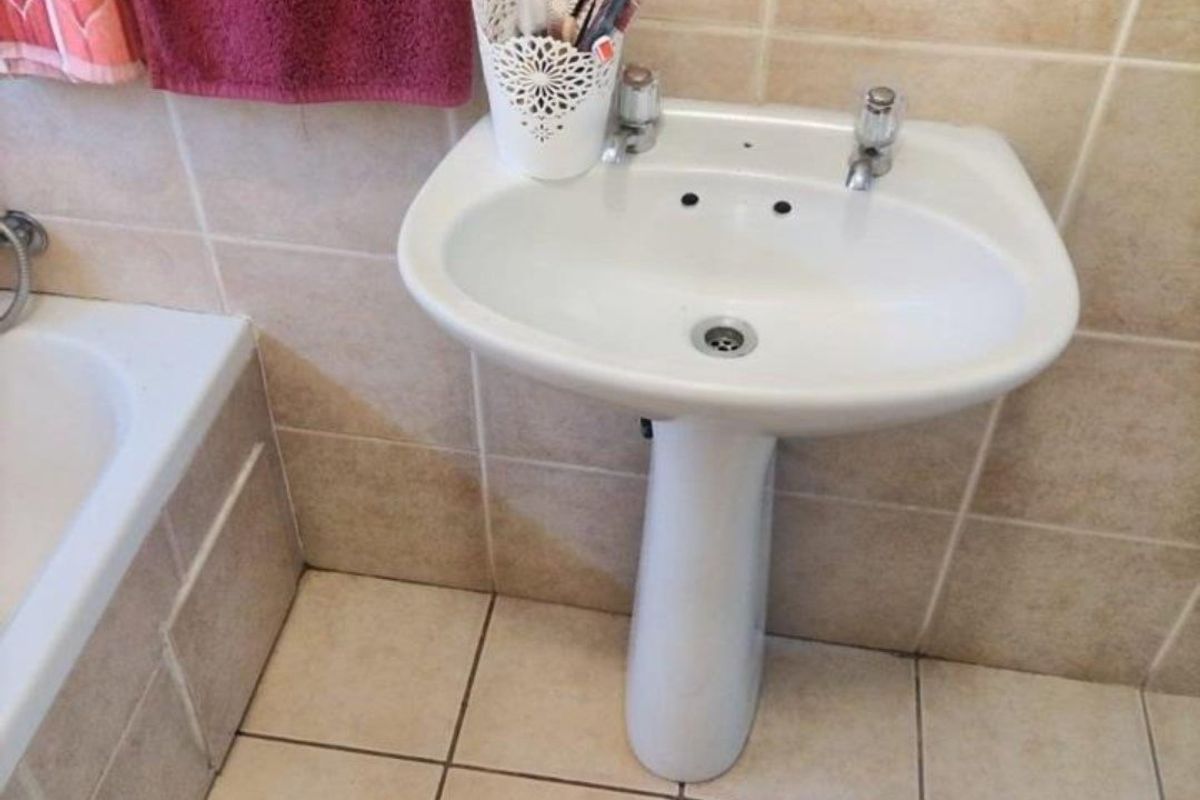 A functional bathroom featuring a white pedestal basin, tiled flooring, and wall tiling, adjacent to a bathtub.