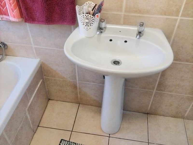 A functional bathroom featuring a white pedestal basin, tiled flooring, and wall tiling, adjacent to a bathtub.