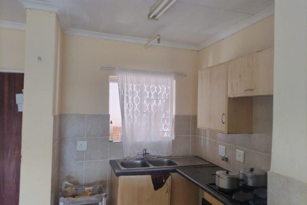 A functional kitchen featuring laminate cabinetry, a double bowl sink, and a tiled splashback, offering a practical layout for daily meal preparation.