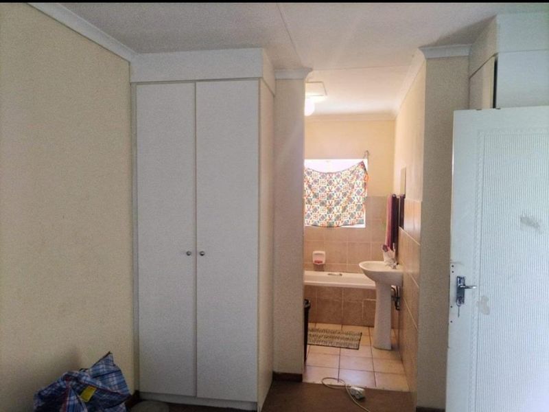 A functional bathroom featuring a pedestal washbasin, bathtub, and built-in storage cupboard, requiring cosmetic updates to improve its overall condition.