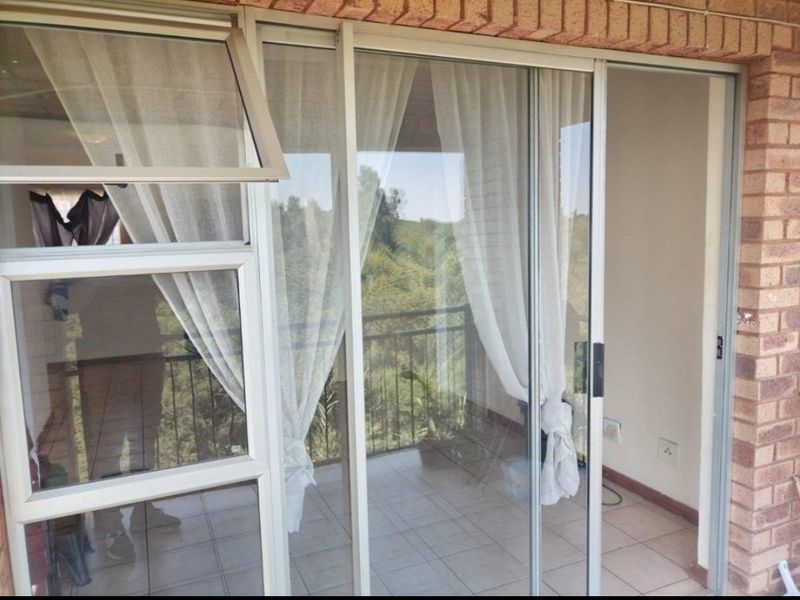 A balcony area featuring tiled flooring, aluminium sliding doors, and a metal balustrade with views of the surrounding greenery.