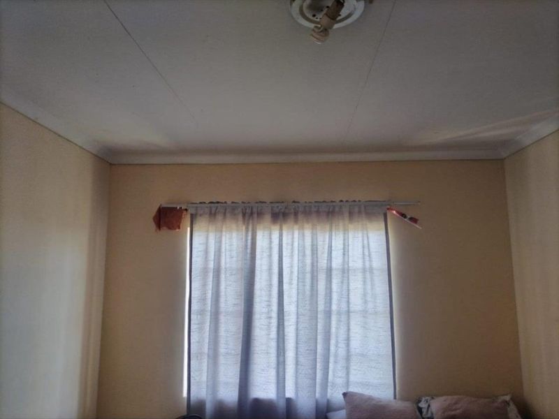 A simple bedroom interior featuring a window with a curtain rod and a ceiling light fixture.