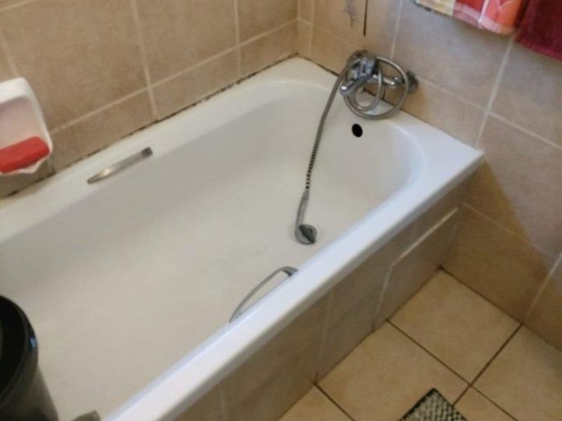 A functional bathroom featuring a standard bathtub with a handheld shower mixer, finished with neutral ceramic wall and floor tiles.