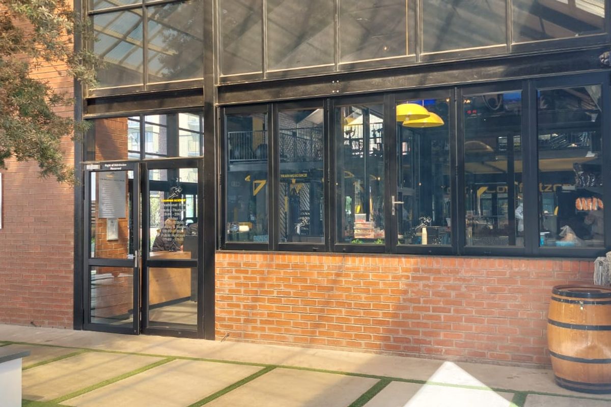 Exterior view of a modern industrial-style building featuring exposed brickwork, large black-framed windows, and a glass atrium roof overlooking a paved courtyard.