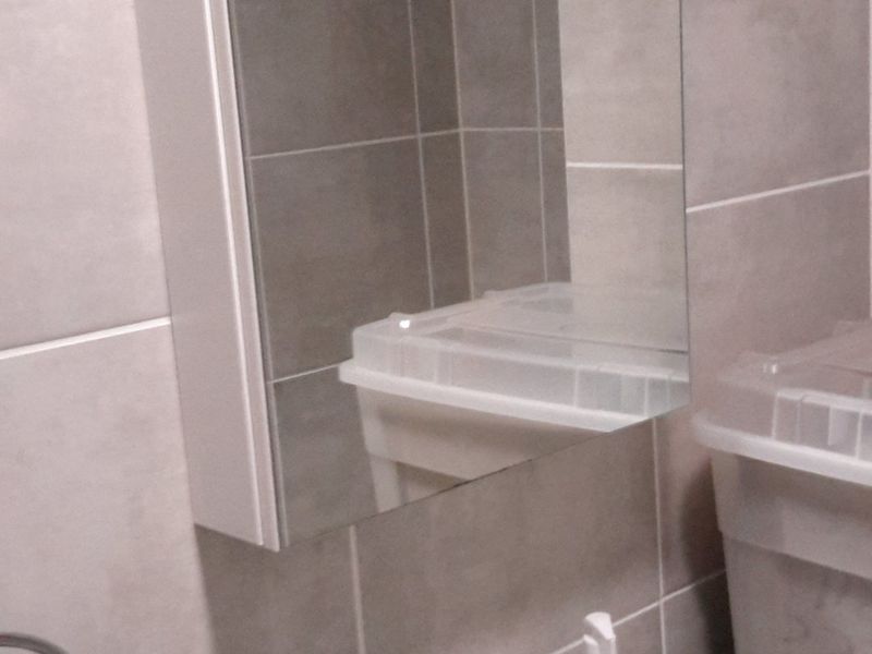 A functional bathroom featuring a ceramic basin with a chrome mixer tap, tiled walls, and a wall-mounted mirror cabinet.