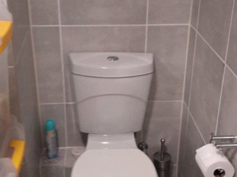 A compact bathroom featuring neutral ceramic wall and floor tiling and a modern dual-flush toilet.