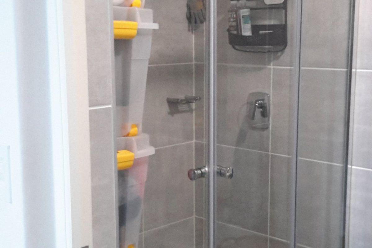 A functional bathroom shower area featuring a glass-enclosed shower cubicle with modern grey wall tiling and a tiled floor.