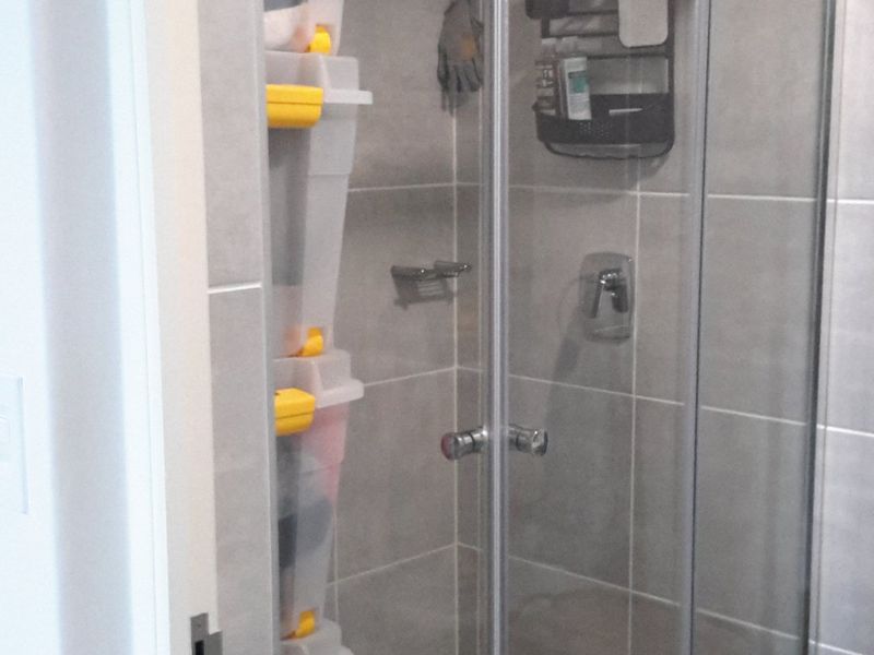 A functional bathroom shower area featuring a glass-enclosed shower cubicle with modern grey wall tiling and a tiled floor.