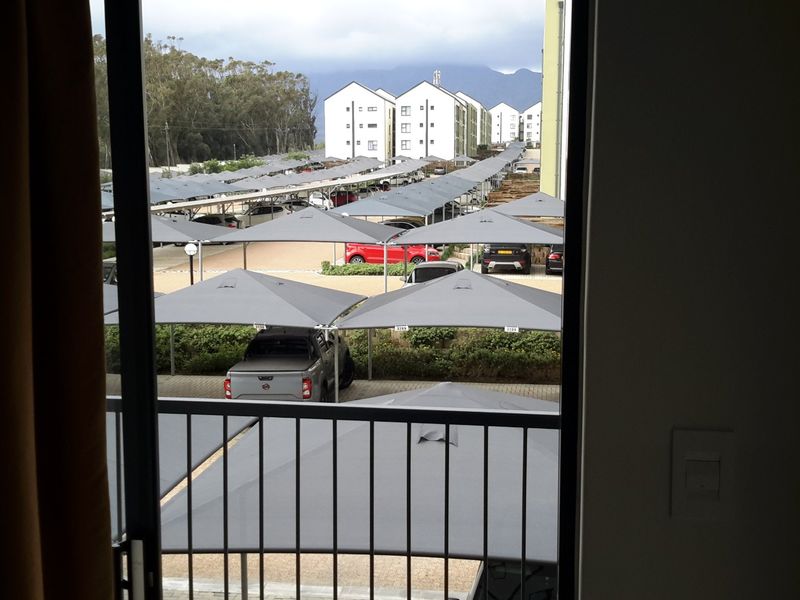 View from an apartment balcony overlooking a complex parking area with covered carports and surrounding residential buildings.