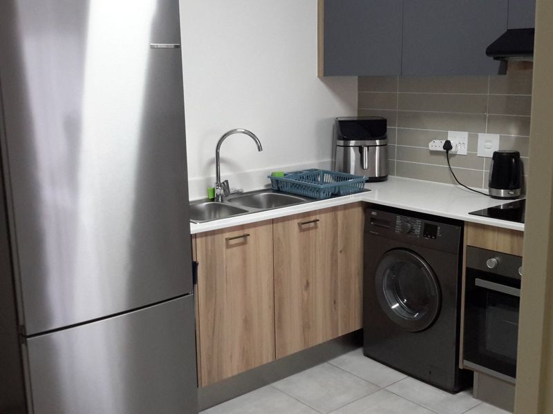 A modern, compact kitchen featuring wood-finish cabinetry, stone countertops, a built-in oven, hob, extractor fan, and integrated laundry appliance space.