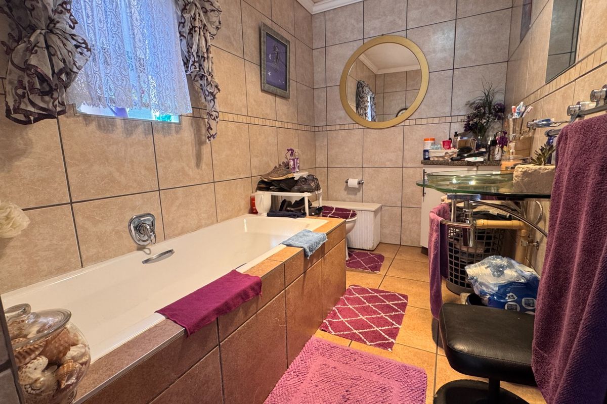 A functional bathroom featuring a built-in bathtub, tiled wall and floor finishes, and a glass vanity basin with a wall-mounted mirror.