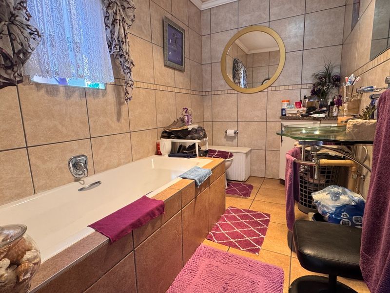 A functional bathroom featuring a built-in bathtub, tiled wall and floor finishes, and a glass vanity basin with a wall-mounted mirror.