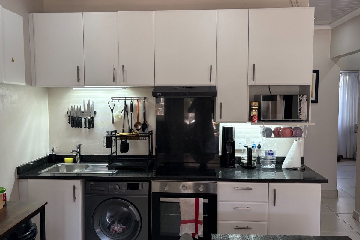 A compact, functional kitchen featuring white cabinetry, granite countertops, integrated oven, extractor fan, and a built-in washing machine.