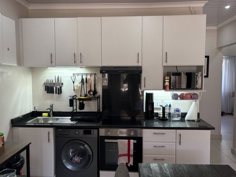 A compact, functional kitchen featuring white cabinetry, granite countertops, integrated oven, extractor fan, and a built-in washing machine.