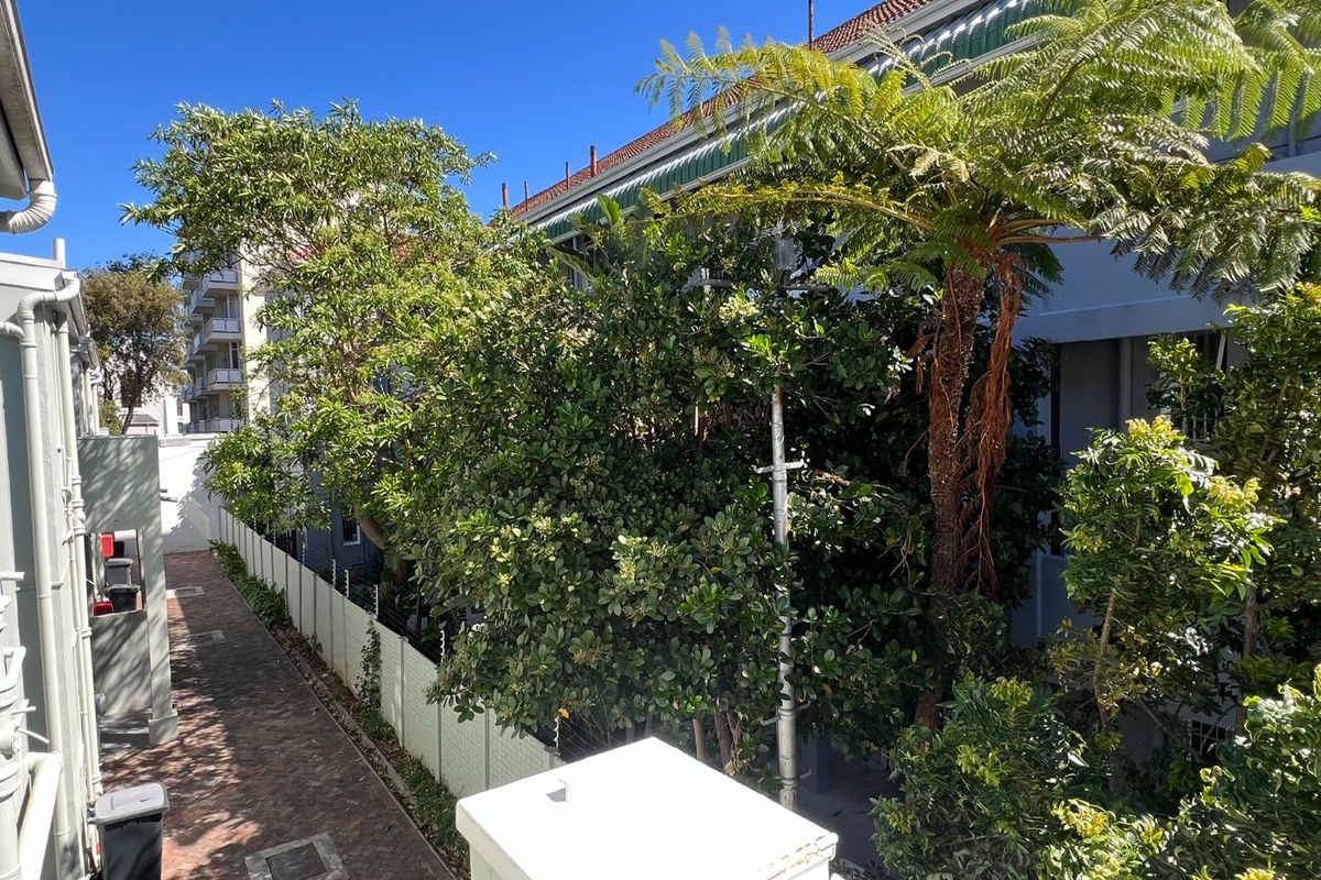 A view of the rear exterior area featuring brick paving, perimeter fencing, and mature landscaping alongside the building structure.