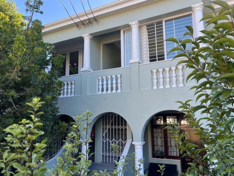 A two-story apartment building facade featuring arched ground-level entryways, a balcony with balustrades, and classic column detailing.