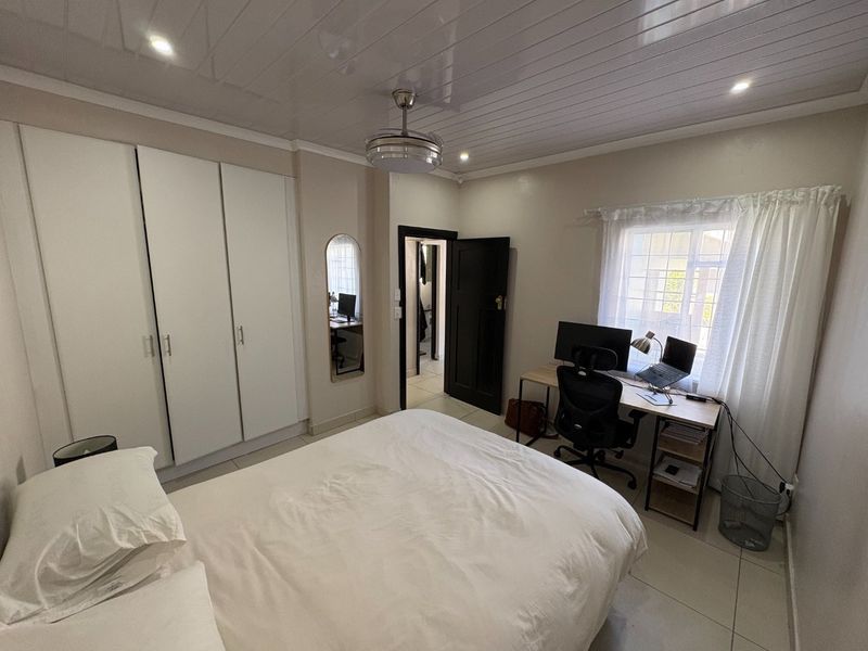 A well-maintained bedroom featuring built-in cupboards, tiled flooring, a ceiling fan, and a window with security bars, providing a functional and comfortable living space.