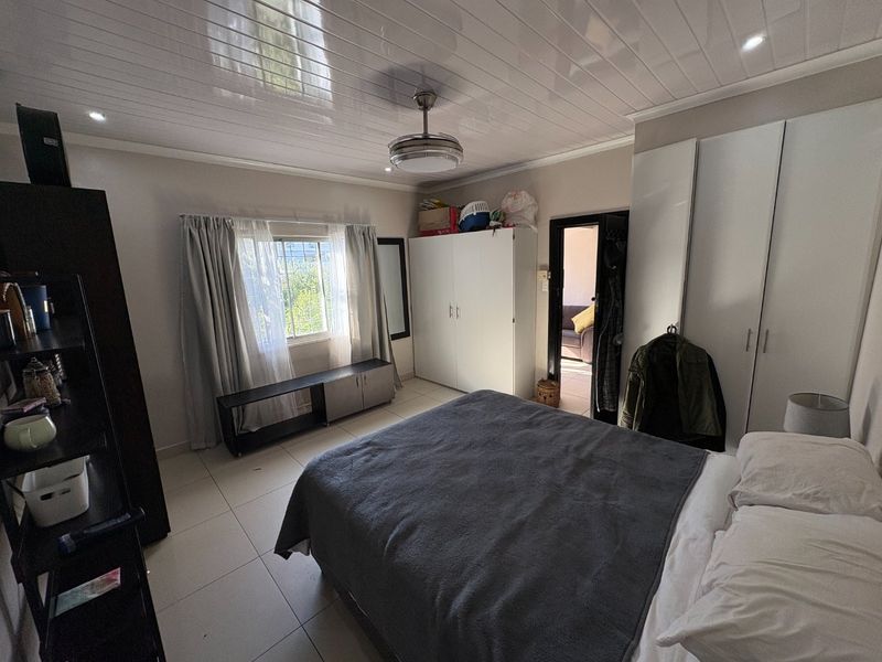 A bedroom featuring tiled flooring, built-in cupboards, a ceiling fan, and recessed lighting, offering a functional space with natural light.