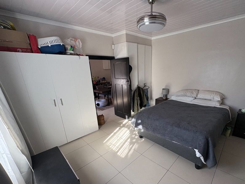 A bedroom featuring tiled flooring, built-in cupboards, and a ceiling fan, with a view into an adjacent living area.