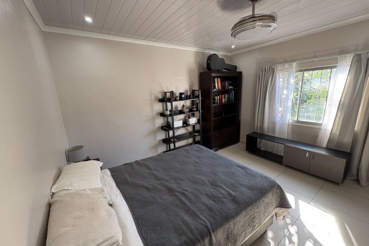 A bedroom featuring tiled flooring, a ceiling fan, and a window with security bars, providing a functional and well-lit living space.