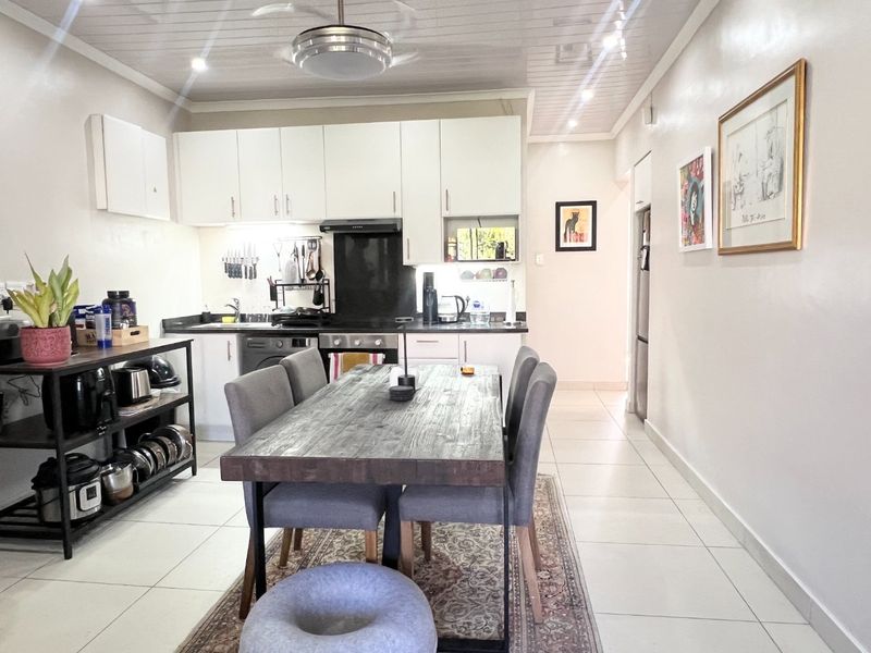 An open-plan kitchen and dining area featuring white cabinetry, tiled flooring, and modern recessed lighting, creating a functional and bright living space.