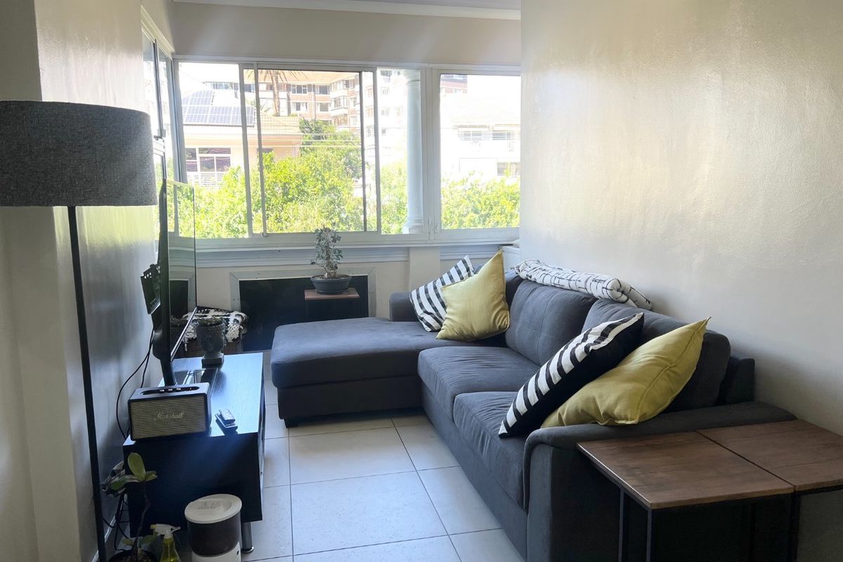 A bright living room featuring tiled flooring and large windows that provide natural light and an urban view.