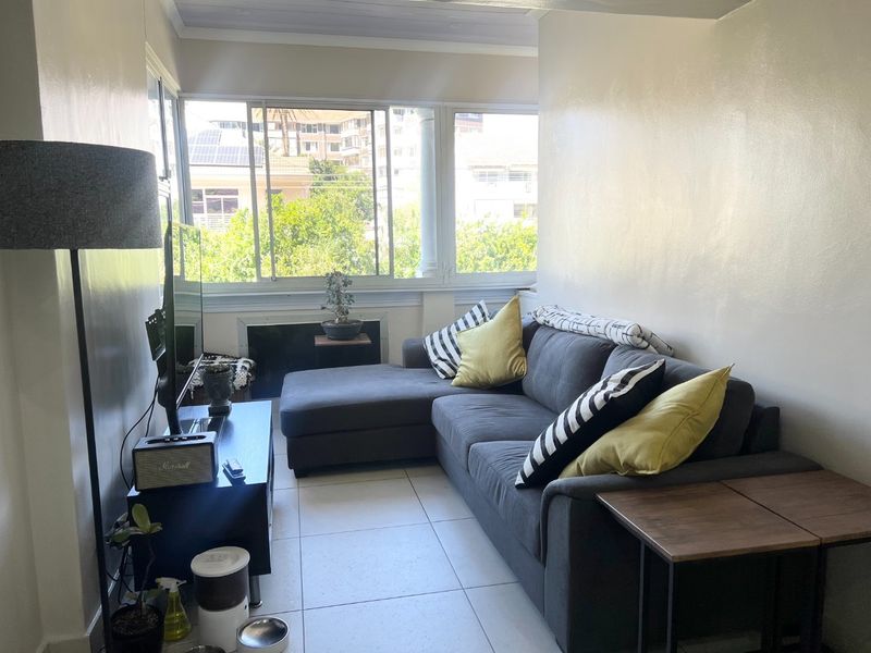 A bright living room featuring tiled flooring and large windows that provide natural light and an urban view.