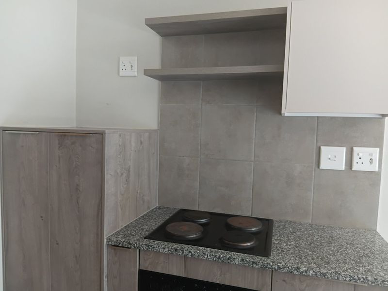 A modern kitchen area featuring built-in cabinetry, granite countertops, an electric hob, and a tiled backsplash with open shelving.