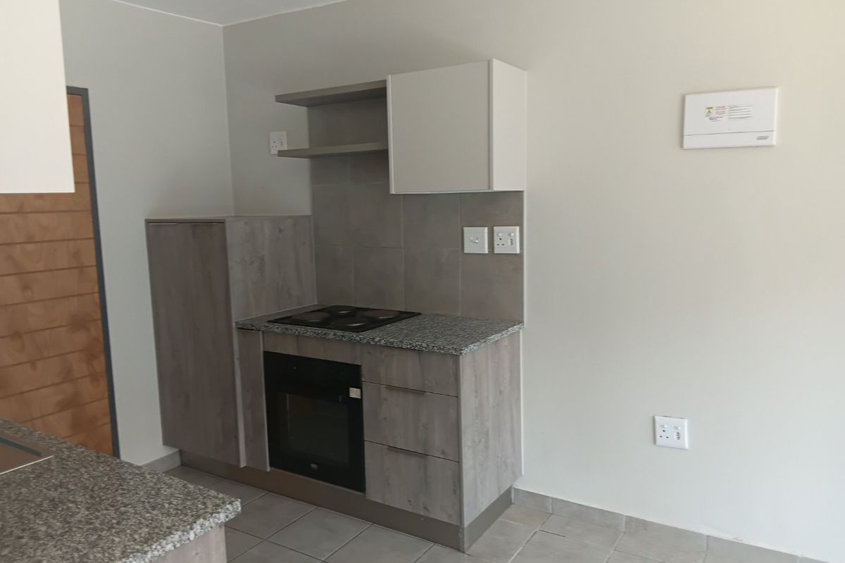 A clean, modern kitchen featuring built-in cabinetry, granite countertops, an integrated oven and hob, and neutral tiled flooring.