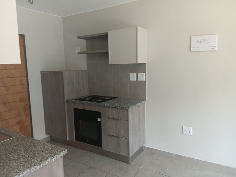 A clean, modern kitchen featuring built-in cabinetry, granite countertops, an integrated oven and hob, and neutral tiled flooring.
